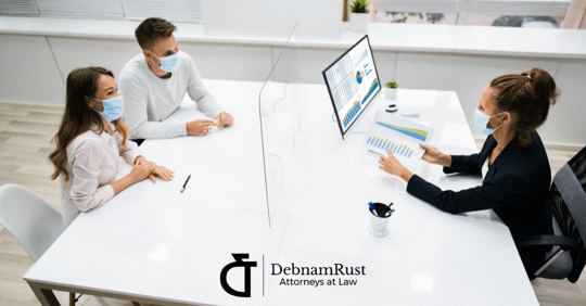 people with masks sitting across the table from a lawyer