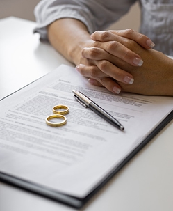 Three people in formal attire reviewing divorce documents at a desk, with a bronze Lady Justice statue centered between them, symbolizing law and fairness during the divorce process.