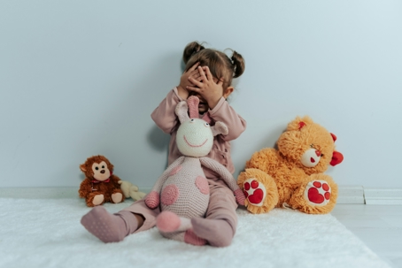 Young child sitting with stuffed animals covering face during family custody stress concept